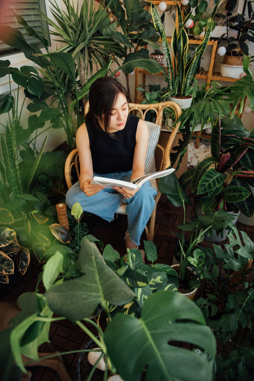 Photo by Kailun Zhang Woman reading a book surrounded by lush green plants.